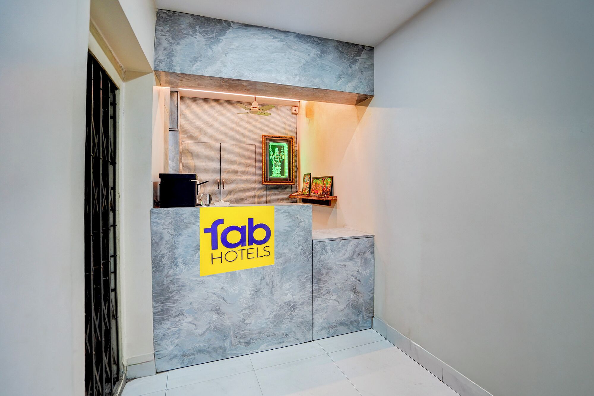 Zona de recepción de hotel con pared de mármol, mostrador de recepción, una obra de arte enmarcada y un cartel que dice 'fab hotels'.