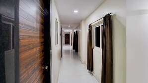 Un pasillo con puerta de madera, ventana con cortinas y suelo de baldosas.