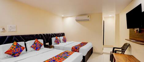 A hotel room with two beds, a wooden table, a chair, an air conditioning unit, and a television mounted on the wall.