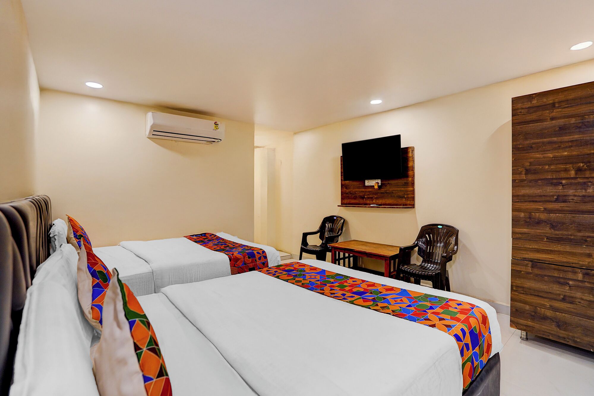 Habitación de hotel con dos camas, un escritorio, una silla, un equipo de aire acondicionado y una televisión en la pared.