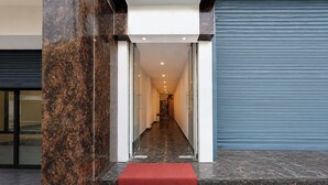 Entrada de hotel com um pilar de mármore, escada com carpete vermelho e porta com persiana azul.
