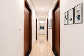A hallway with wooden doors, a marble floor, and framed artwork on the walls. - FabHotel Ostan Stayz 15 - Noida Sector-15 (Noida)
