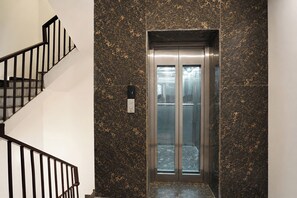 An elevator with a metallic finish, a marble wall with a speckled pattern, and a black metal staircase with a handrail. - FabHotel Ostan Stayz 15 - Noida Sector-15 (Noida)