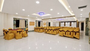 A conference room with rows of chairs, a stage, and a ceiling with recessed lighting. - FabHotel Prime The City Park (Hyderabad)