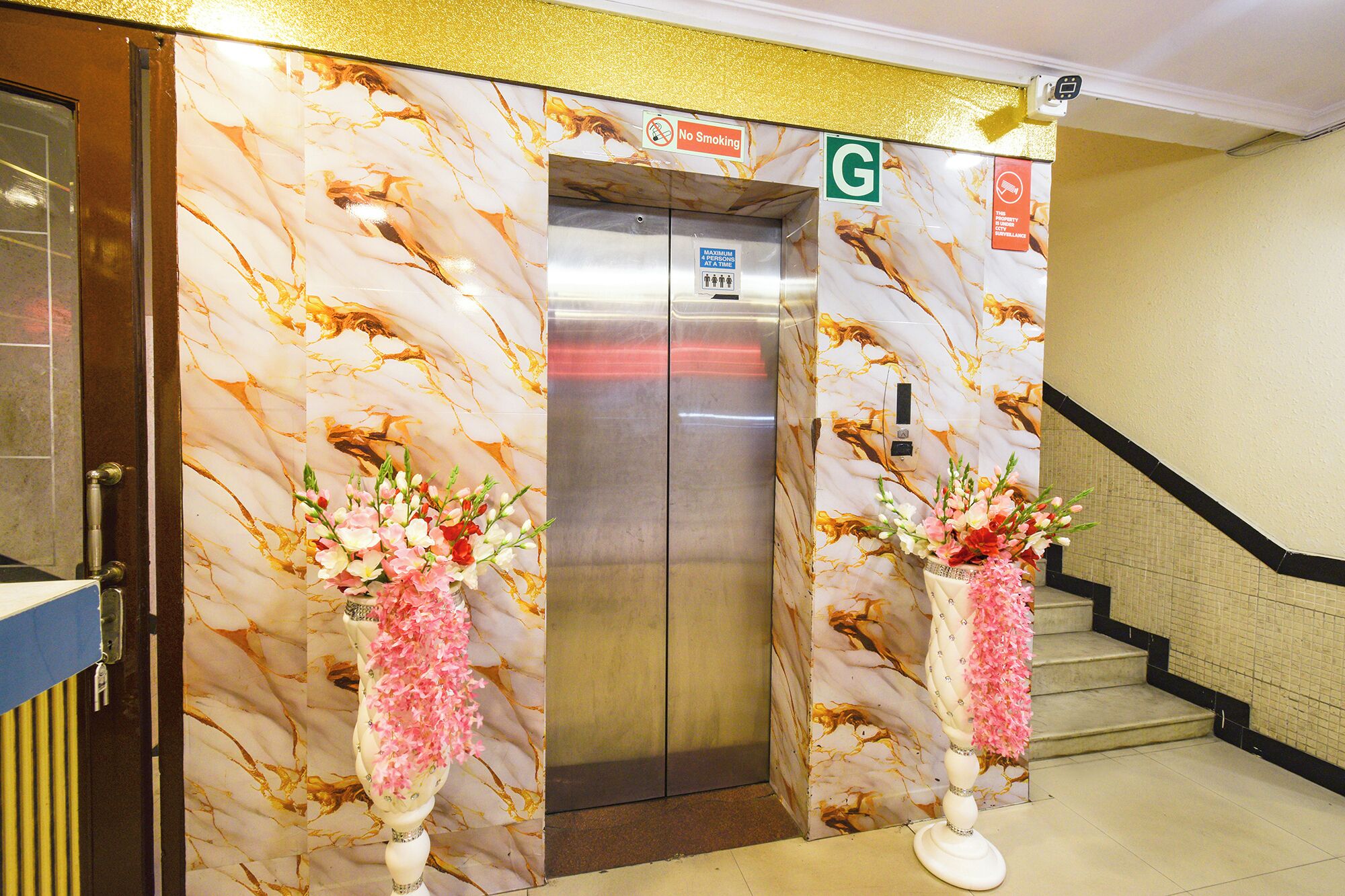 An elevator with a marble wall design, a 'No Smoking' sign, a 'G' gender designation sign, and two flower arrangements.