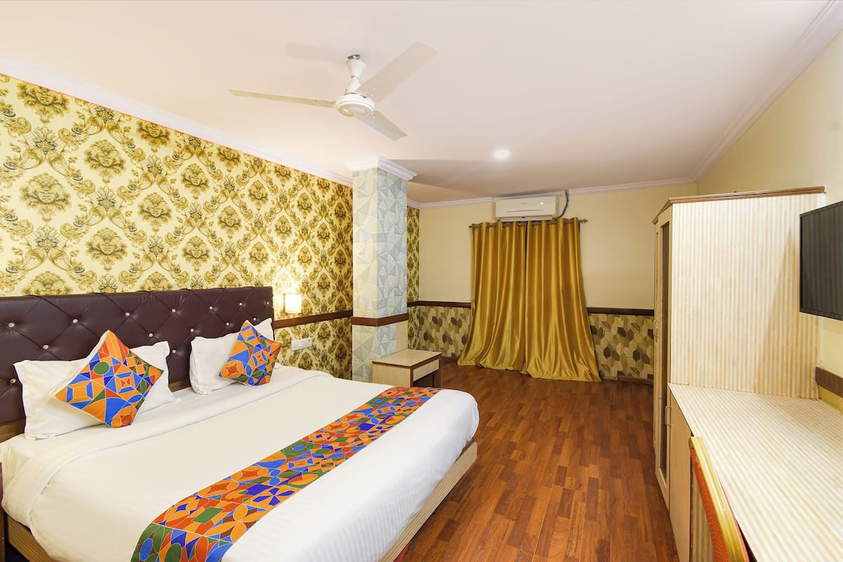 A hotel room with a bed, a TV, a ceiling fan, and a window with curtains.