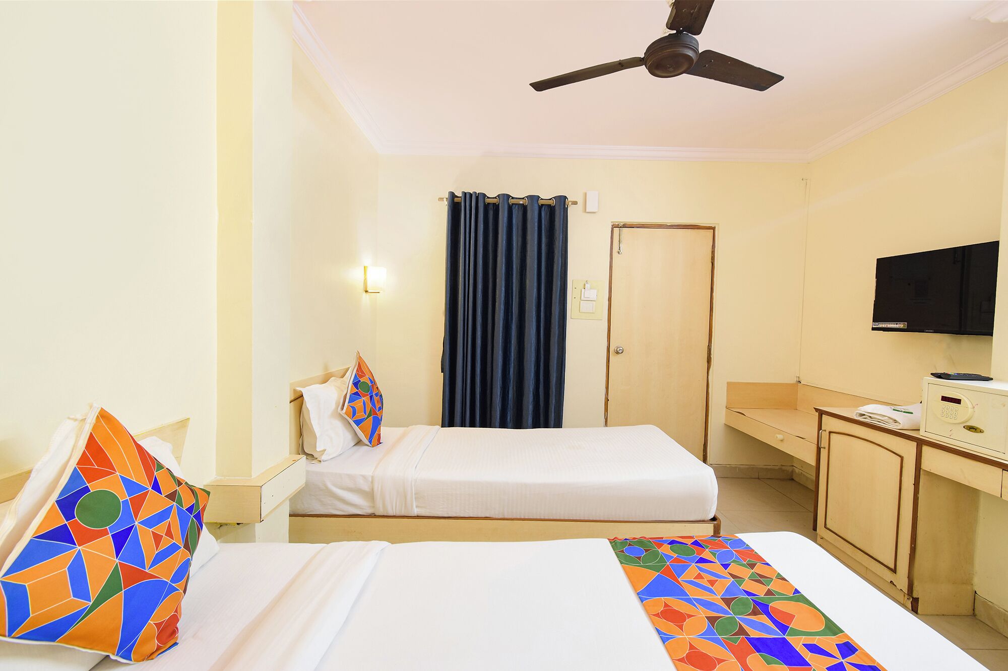 Una habitación de hotel con cama, escritorio, televisor y ventilador de techo.