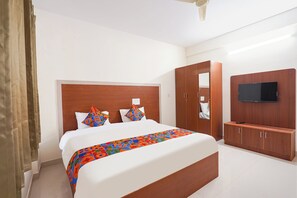 Hotellihuone, jossa on suuri sänky, puinen pääty, seinälle asennettu televisio ja vaatekaappi.