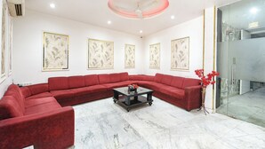 A modern living room with a red sectional sofa, a glass door leading to a balcony, and four framed botanical prints on the wall. - Fabhotel Perfectionist (New Delhi)