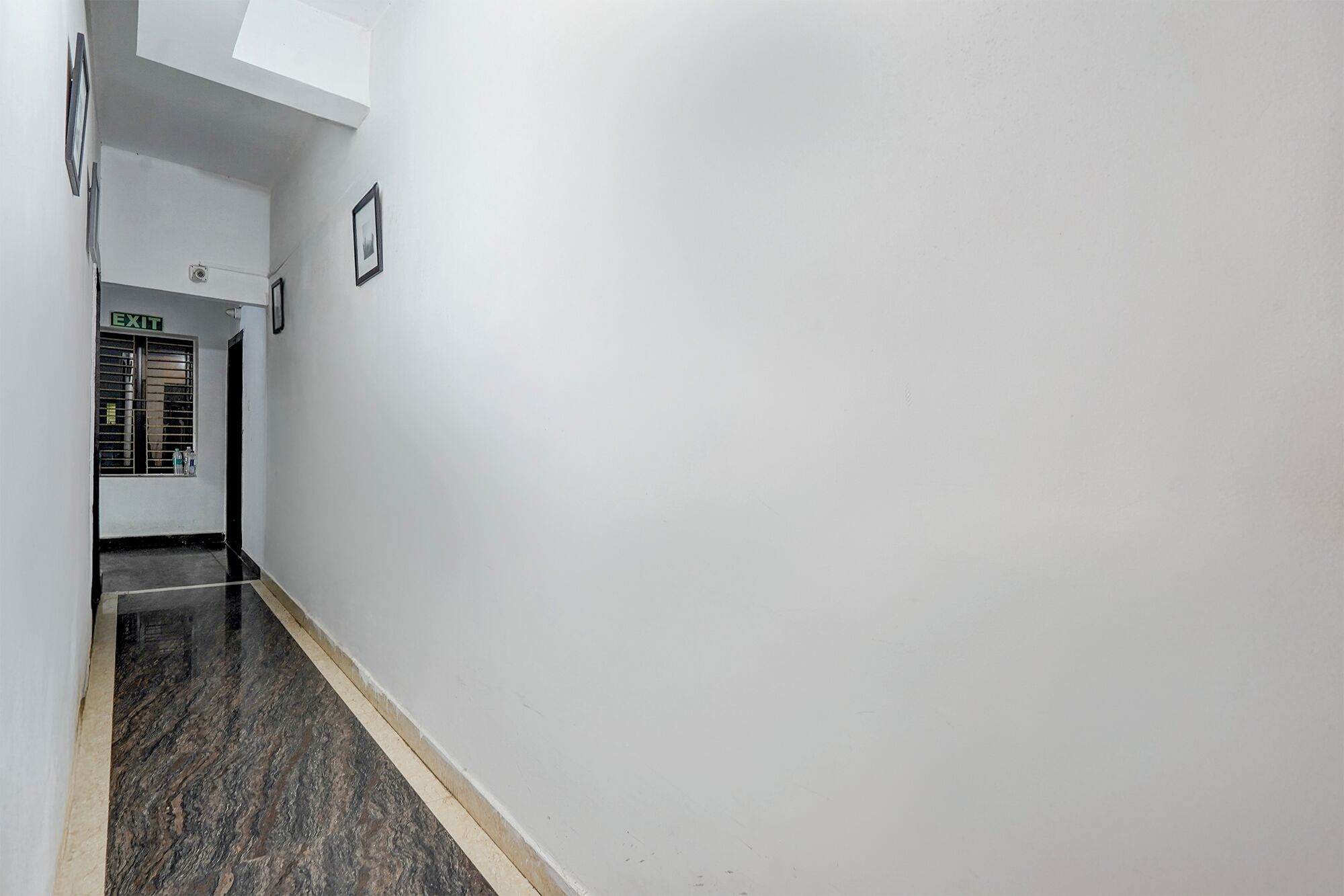 A hallway with a white wall, a door with an exit sign, and a tiled floor.
