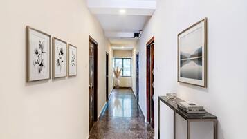 Un pasillo con obras de arte enmarcadas en las paredes, piso de mármol y vista a otra habitación.