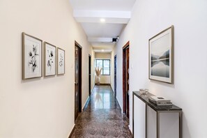 Un pasillo con obras de arte enmarcadas en las paredes, piso de mármol y vista a otra habitación.