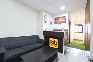 A hotel reception area with a sofa, a coffee table, a reception desk, a clock, a TV, and a 'No Smoking' sign. - Fabhotel Akshay Inn (Pune)