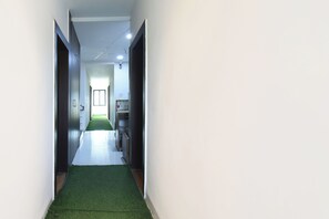 A hallway with a green carpet, white walls, and a door on the left. - Fabhotel Akshay Inn (Pune)