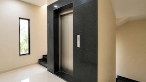 A modern elevator with a black marble finish, a small window, and a control panel with a number 2 button. - FabHotel Grand Villa (Indore)