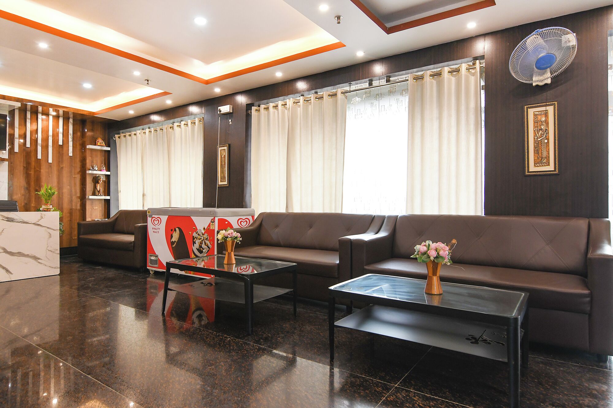 Um lobby moderno com balcão de recepção, sofás de couro, mesa de centro de vidro e uma grande janela com cortinas.