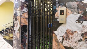 Un ascensor moderno con pared de mármol, puerta metálica y panel de control con una luz roja.