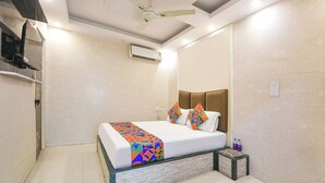 Una habitació d'hotel amb un llit, una taula de nit, un aparell d'aire condicionat i un ventilador de sostre.