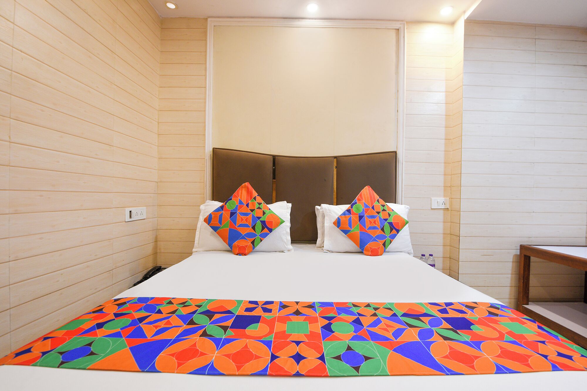 Ein Hotelzimmer mit Bett, Kissen und einer farbenfrohen Bettdecke.