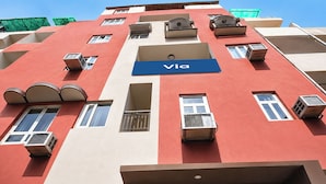 Un edifici de diverses plantes amb façana vermella, un cartell blau amb la paraula 'Via', diversos balcons i aparells d'aire condicionat.