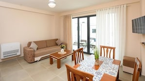 A living room with a sofa, a coffee table, a dining table with chairs, a TV mounted on the wall, and a sliding glass door leading to an outdoor area. - Velaris Apartments (Vlore)