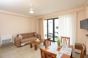 A living room with a sofa, a coffee table, a dining table with chairs, a TV mounted on the wall, and a sliding glass door leading to an outdoor area. - Velaris Apartments (Vlore)