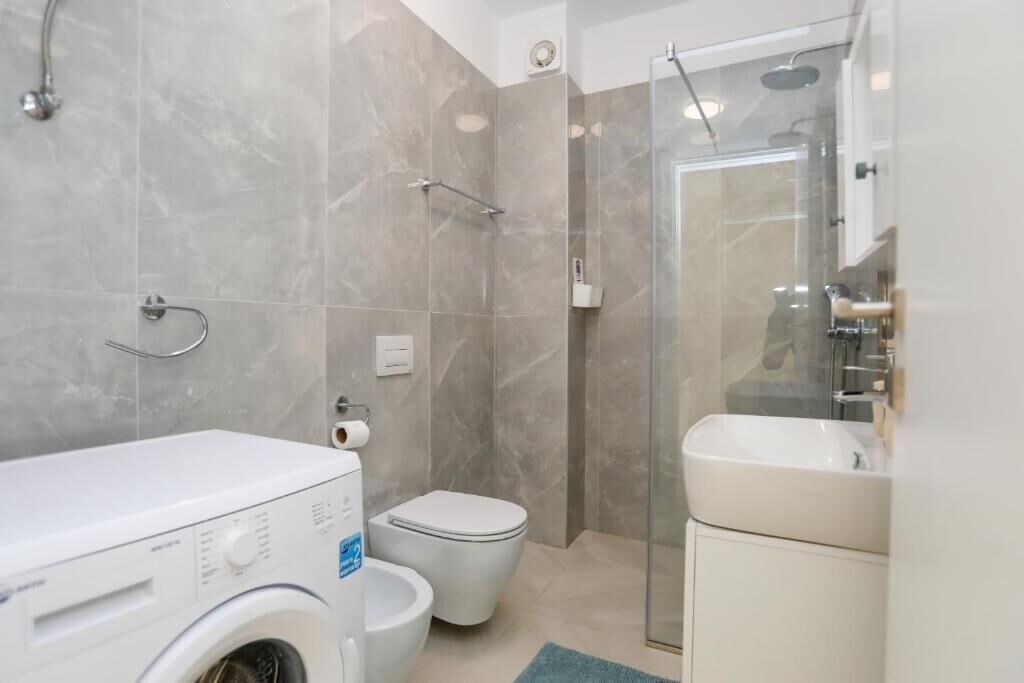 Un bagno dotato di lavatrice, WC, doccia e lavandino.