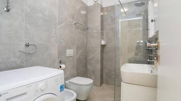 Un bagno dotato di lavatrice, WC, doccia e lavandino.