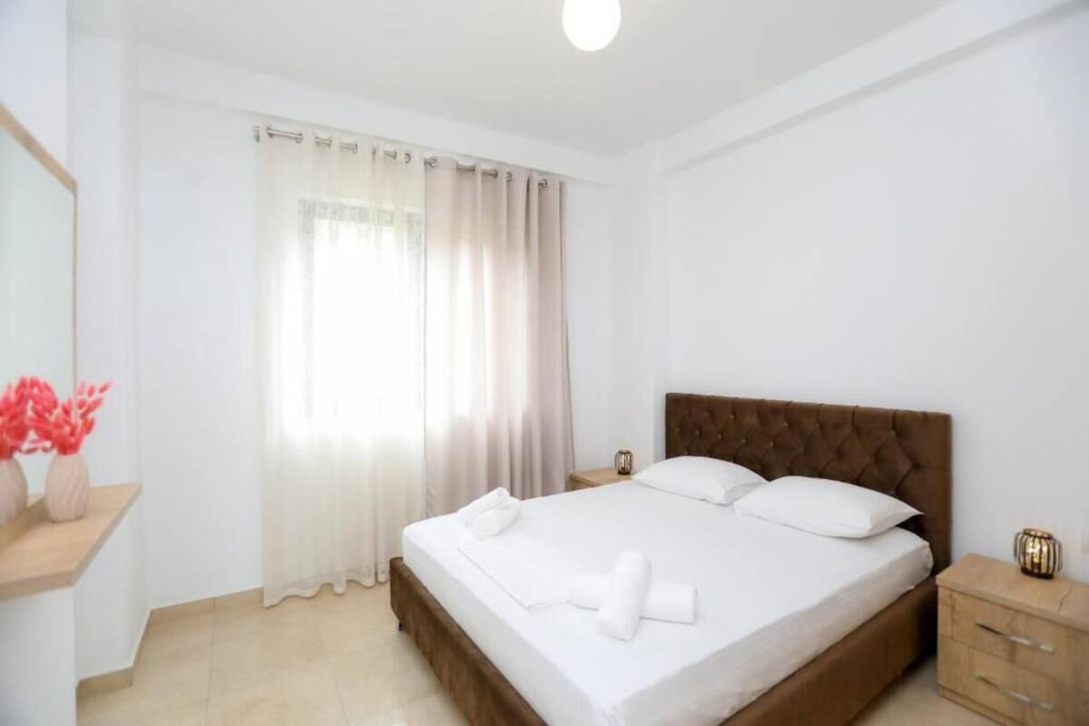 Una habitación de hotel con una cama grande, una mesita de noche y un ventanal con cortinas.