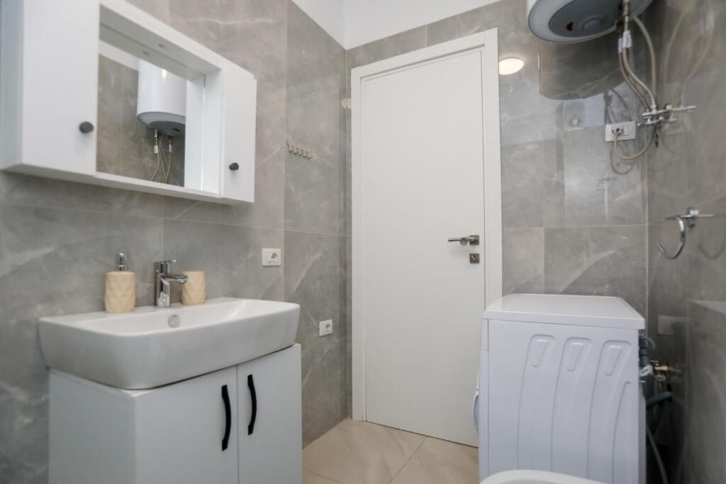 Un baño con lavamanos blanco, un espejo, ducha e inodoro.