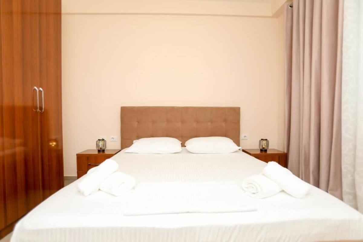 Una cama bien tendida con sábanas blancas, dos mesitas de noche con lámparas y un armario de madera.