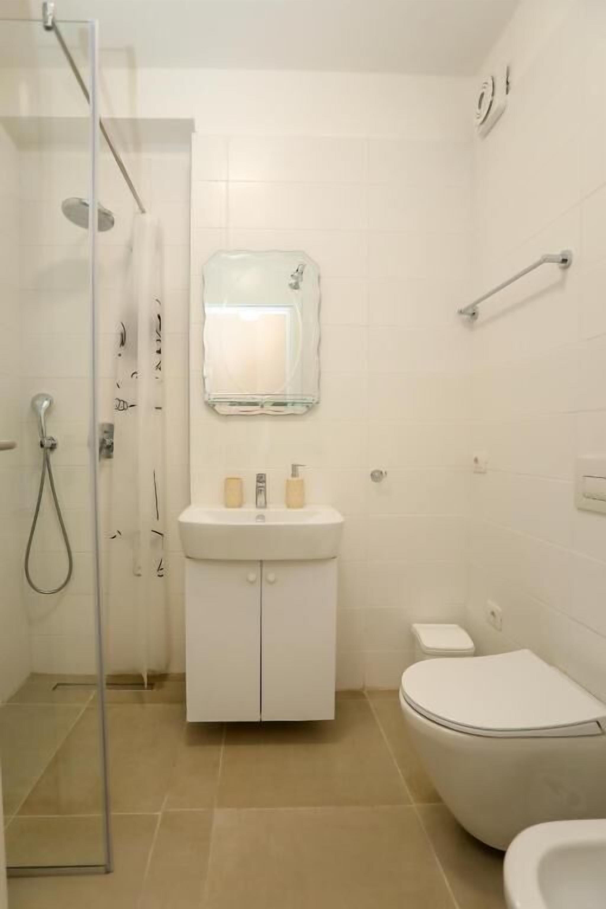 A bathroom with a shower, toilet, sink, and mirror.