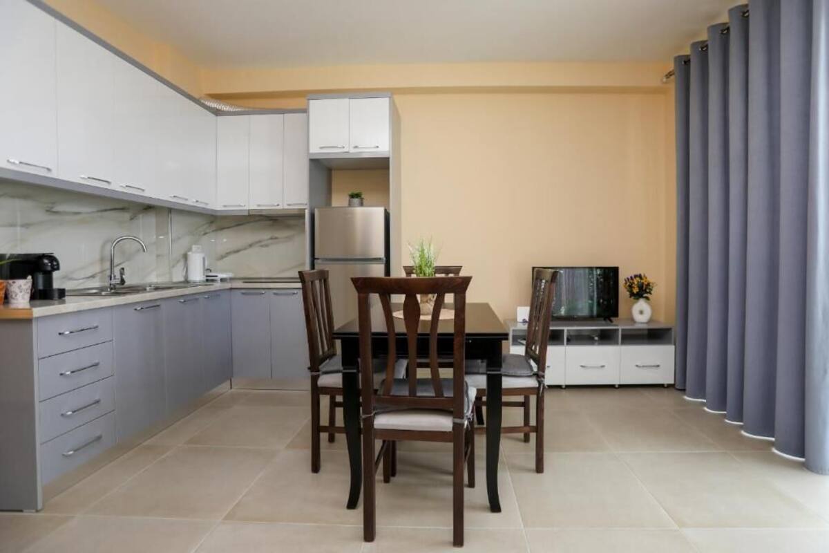 Una cocina moderna con armarios grises, una mesa de comedor con sillas, un televisor y una cortina gris.