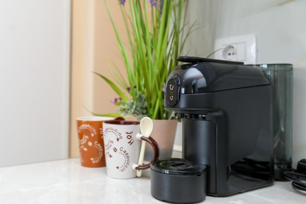 Una cafetera sobre una encimera con una taza de café y una cuchara.