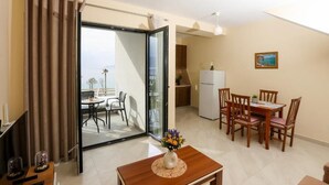 A room with a dining table, chairs, a vase with flowers, a TV, and a sliding glass door leading to a balcony. - Velaris Apartments (Vlore)