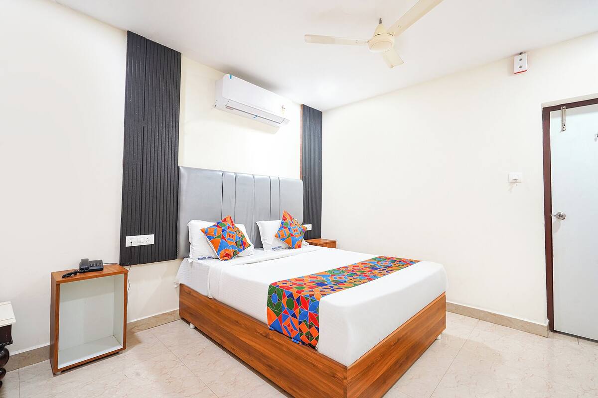 A modern hotel room with a wooden bed, a nightstand, a mirror, a ceiling fan, and an air conditioning unit.
