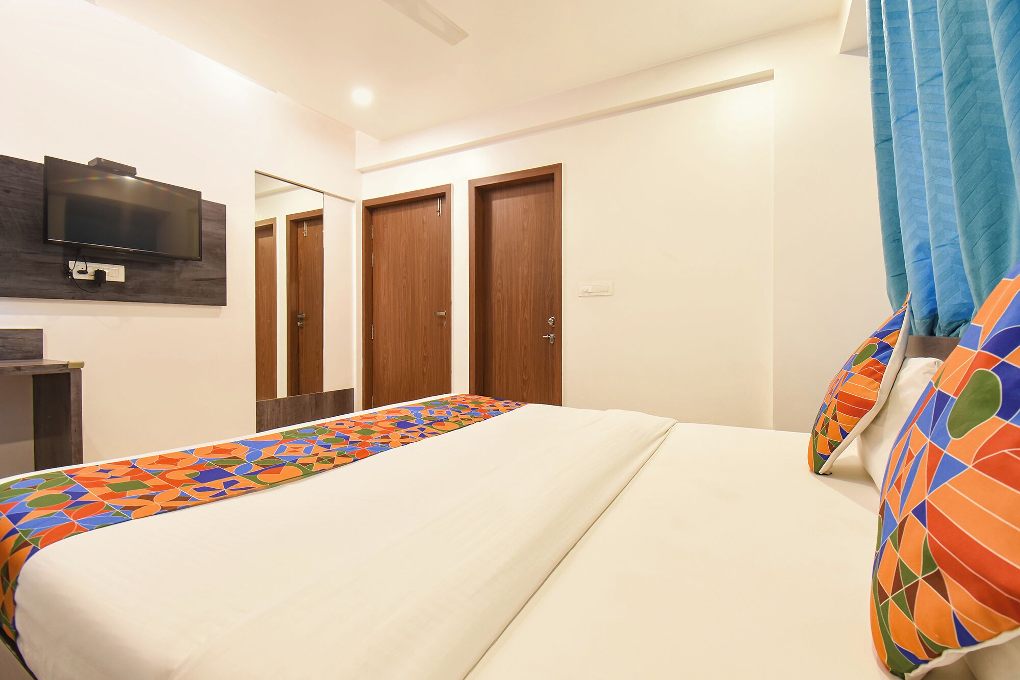 Un dormitorio con una cama, un televisor montado en la pared y un juego de puertas de madera.