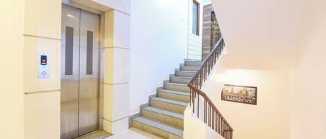 A modern elevator with a digital display, a staircase with a handrail, and a framed picture on the wall.