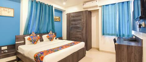 A bedroom with a bed, curtains, a ceiling fan, an air conditioning unit, a desk with a chair, and a television.