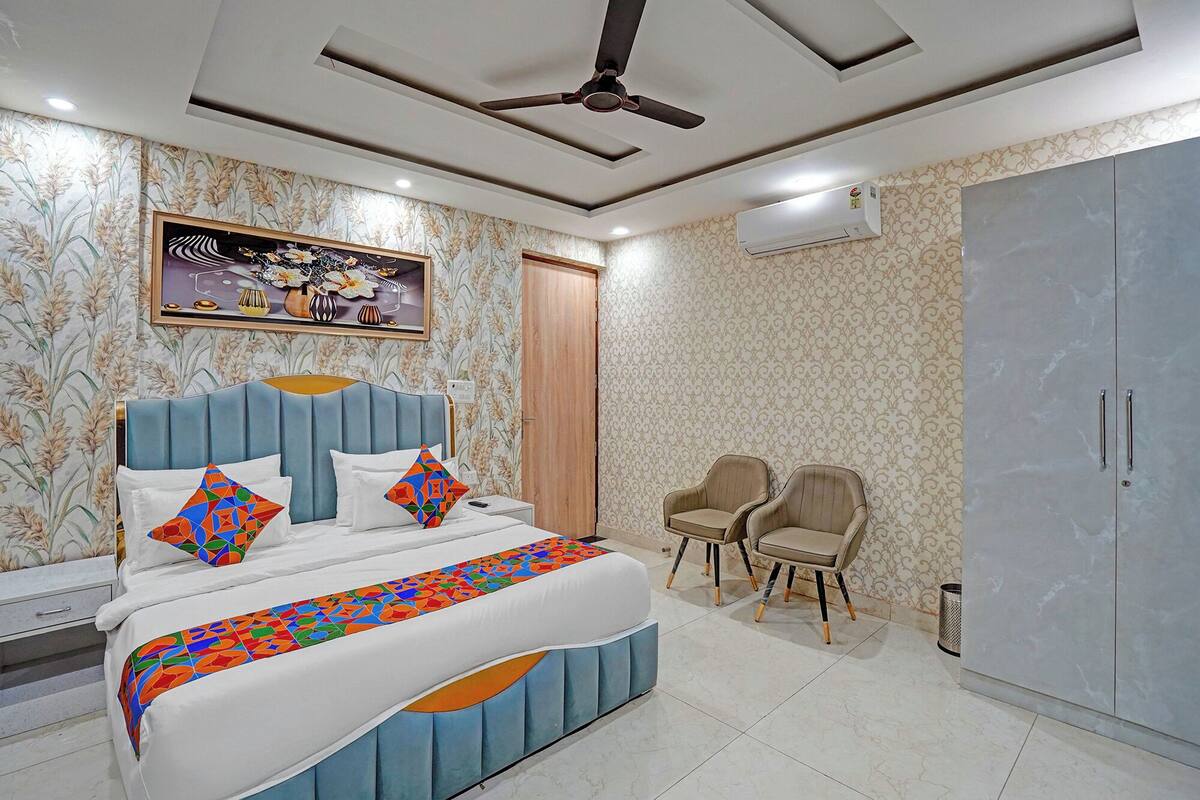 Un dormitorio con cama, dos sillas, armario y aire acondicionado.