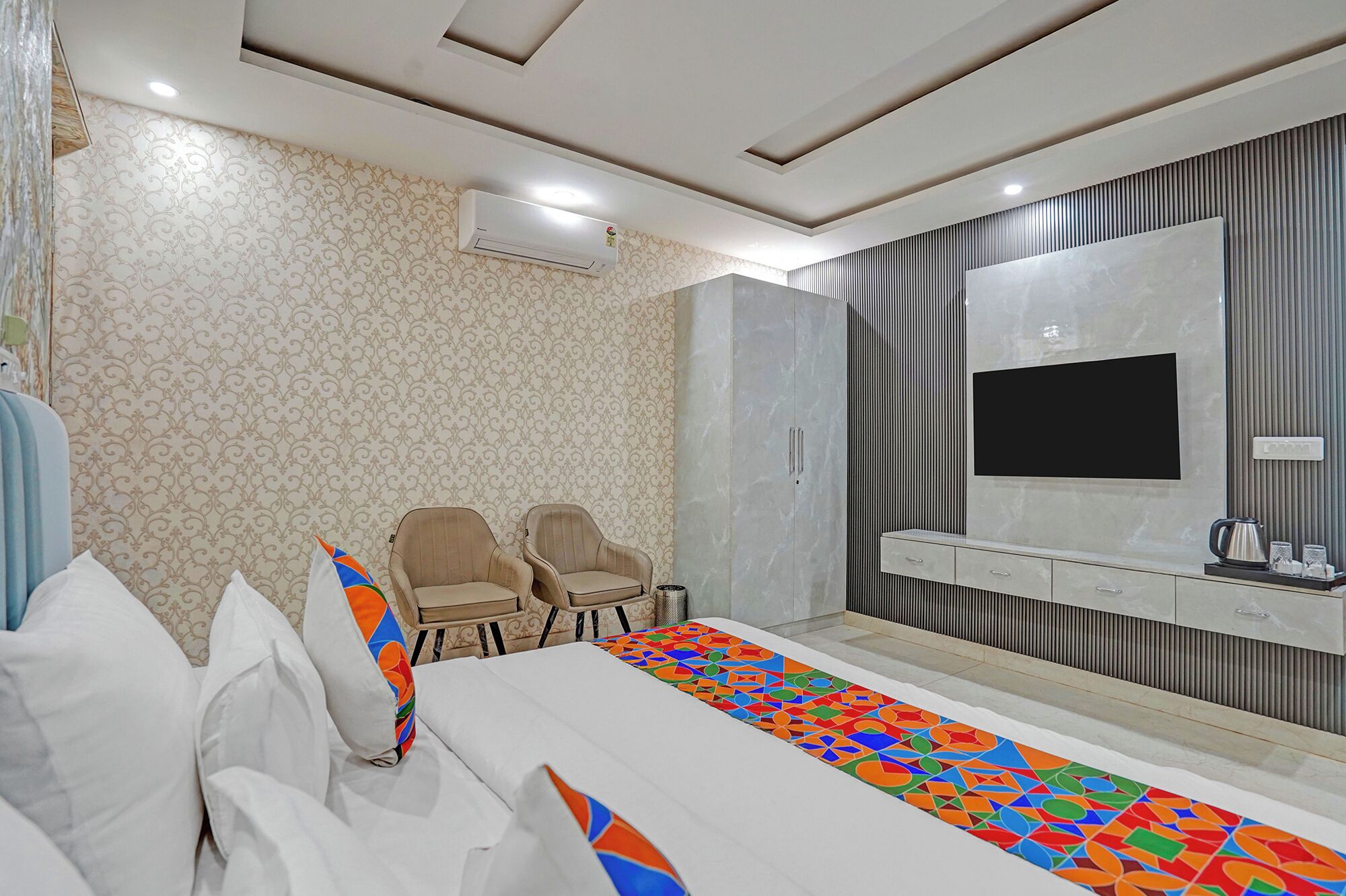 A hotel room with a bed, two chairs, a TV, and a minibar.