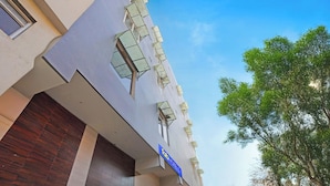Un edificio con un letrero azul que dice 'Tab Hotels', varias ventanas con toldos y un árbol al fondo.