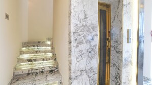Una escalera de mármol que conduce a un cuarto con una puerta de madera y un ascensor de vidrio.