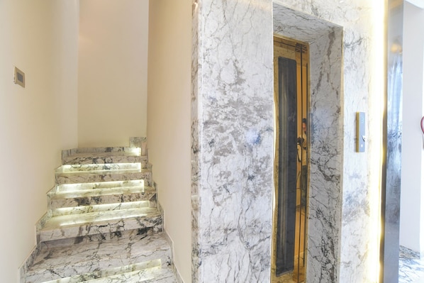 A marble staircase leading to a room with a wooden door and a glass elevator. - FabHotel Raj Villa I, Vijay Nagar (Indore)