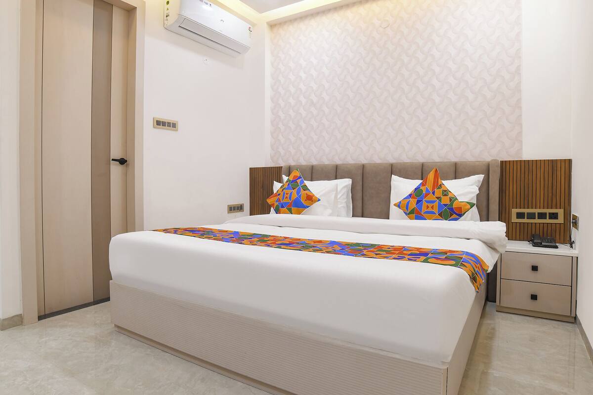Una habitación de hotel con una cama grande, una mesita de noche, aire acondicionado instalado en la pared y un papel tapiz estampado.