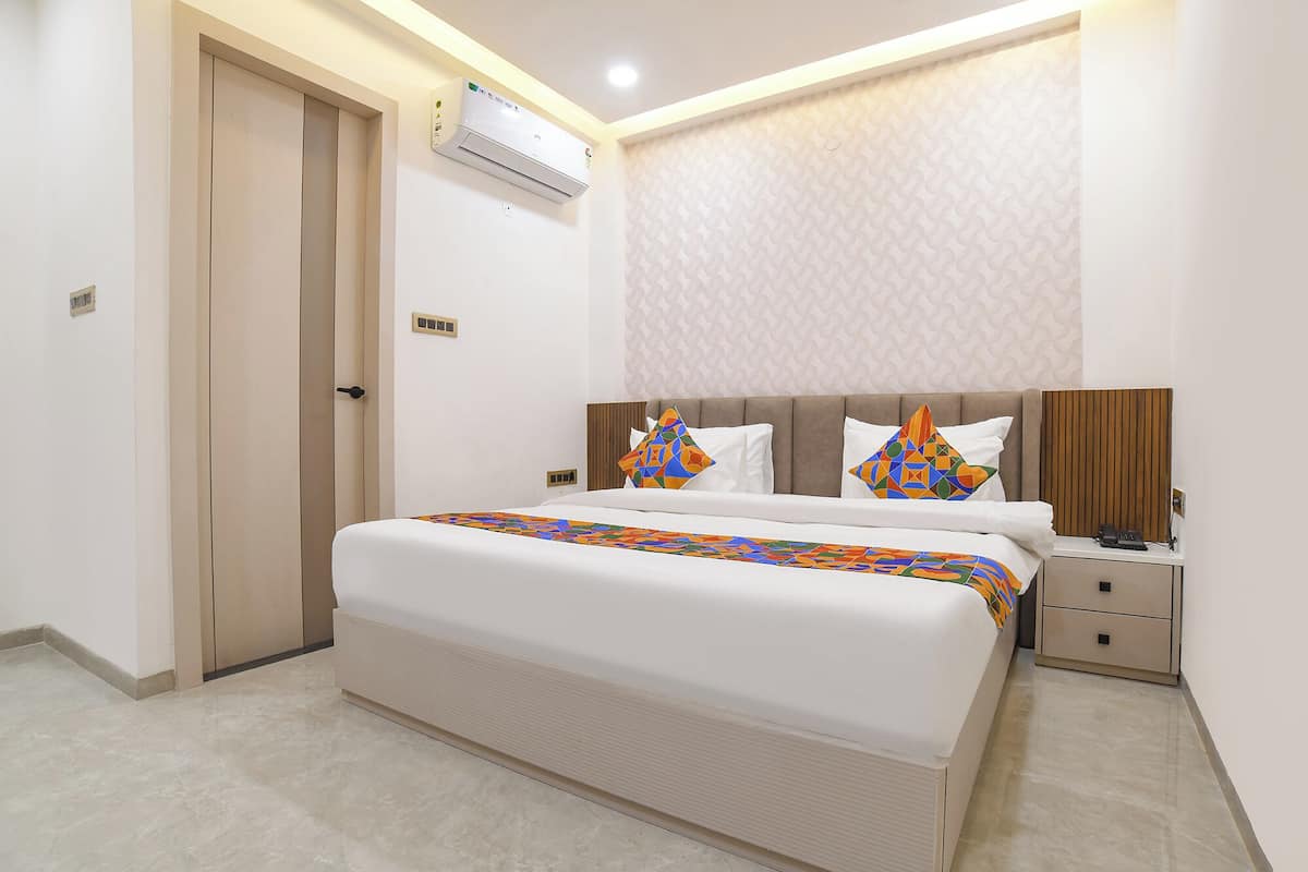 Una habitación de hotel con cama, mesita de noche y unidad de aire acondicionado.