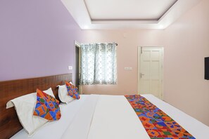 A bedroom with a bed, pillows, a window with curtains, a door, and a wall-mounted light fixture. - FabHotel MR Guest Line - Banashankari (Bangalore)