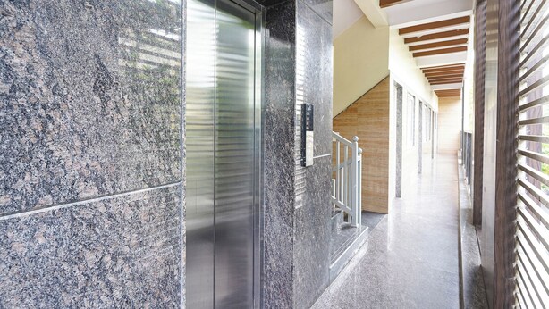 A modern building interior with a marble wall, a glass elevator, and a wooden ceiling. - FabHotel MR Guest Line - Banashankari (Bangalore)