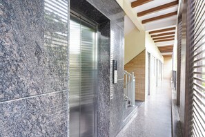 A modern building interior with a marble wall, a glass elevator, and a wooden ceiling. - FabHotel MR Guest Line - Banashankari (Bangalore)