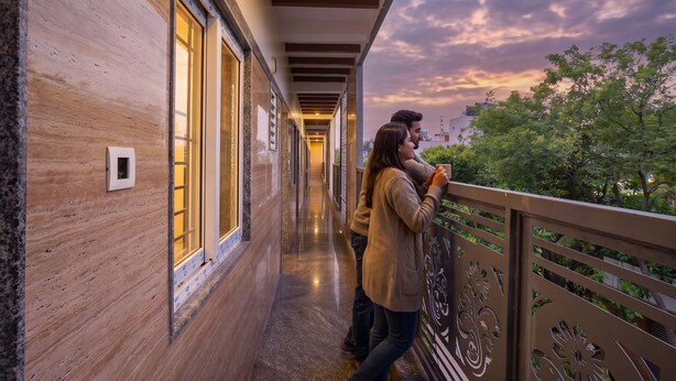 A corridor with wooden walls and large windows, leading to a balcony with decorative railings. - FabHotel MR Guest Line - Banashankari (Bangalore)